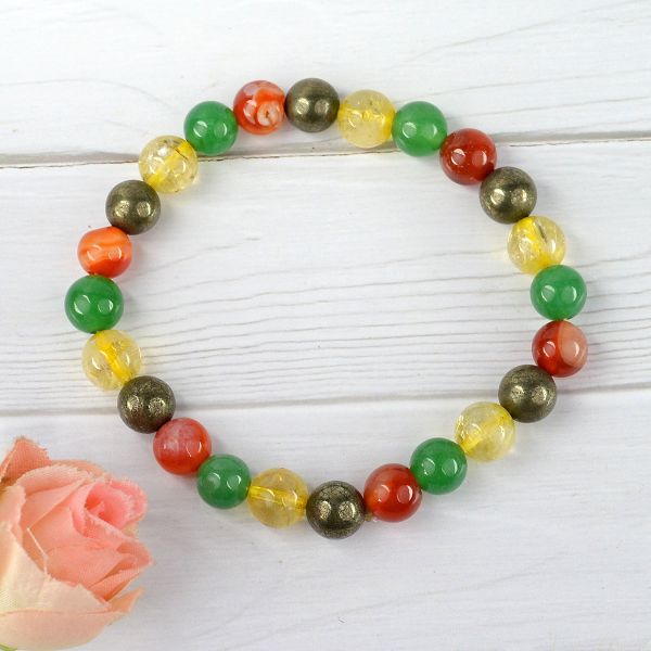 Multicolored beaded bracelet on a white wooden surface with a pink flower.